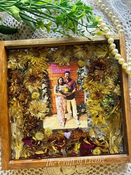 A beautiful shot of the finished 8x8 inch bouquet preservation frame, showing the mix of yellow and red flowers against the couple's photo. The wooden frame adds a rustic, warm touch.