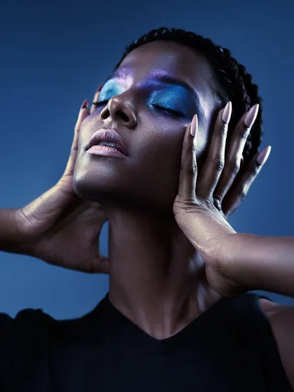 A beauty portrait with vibrant blue eyeshadow against a blue background. The lighting is carefully shaped to highlight the contours of the face and the metallic sheen of the makeup.