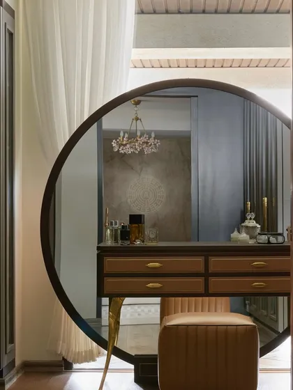 A close-up of the vanity in the master suite, featuring a large round mirror and a delicate floral chandelier reflected in it. The design combines classic elegance with modern forms.