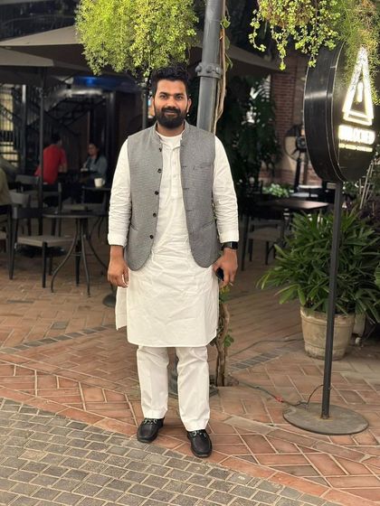 A simple, full-length portrait in a white kurta and grey waistcoat. My style is a blend of traditional roots and modern sensibilities.