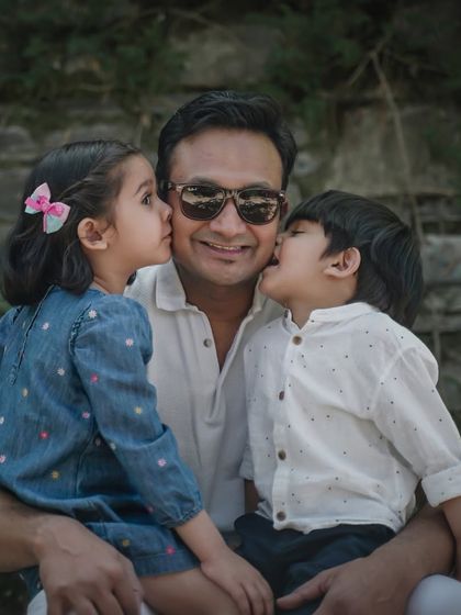 A father gets sweet kisses on both cheeks from his two children during a fun outdoor family portrait session.