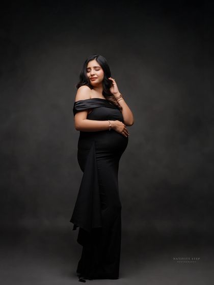 An elegant solo portrait in a form-fitting black off-shoulder gown. The classic pose and dark, moody backdrop create a timeless and sophisticated look.