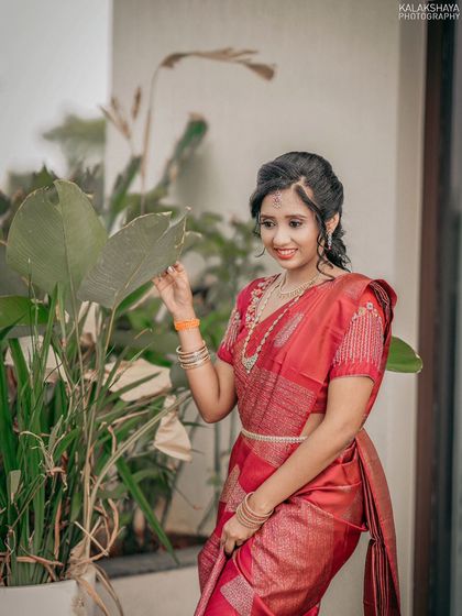 A lovely portrait of a bride in a red saree, posing naturally among plants.