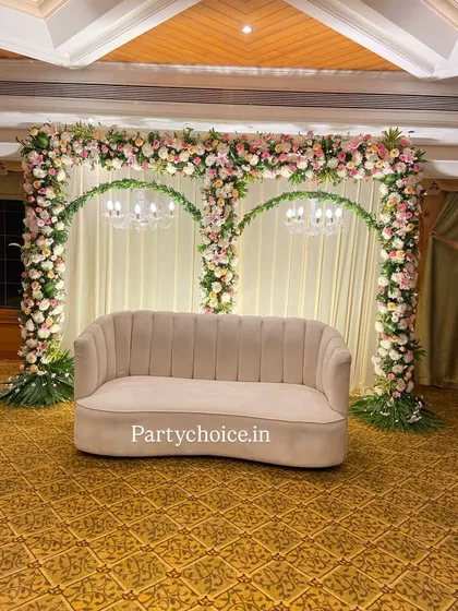 Our engagement stages are designed for elegance and romance. This setup features two graceful floral arches over a modern sofa, set against a clean, draped backdrop with soft lighting, creating a perfect photo opportunity for the couple.