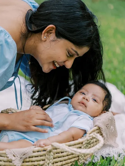 A mother smiling down at her baby, who is nestled in a basket outdoors. This shows the versatility of a lifestyle session, moving from indoors to a garden.