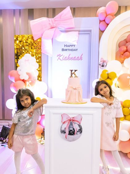 The two birthday girls posing by their elegant, bow-themed birthday cake and backdrop. The design is chic, modern, and perfect for a stylish princess party.