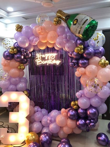 A chic birthday setup in shades of purple and peach, with a large champagne bottle balloon for a fun, celebratory touch.