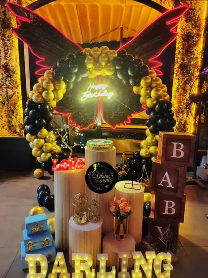 A dramatic birthday setup with black and gold balloons and large, glowing wings. This is a unique and bold choice for a memorable celebration.