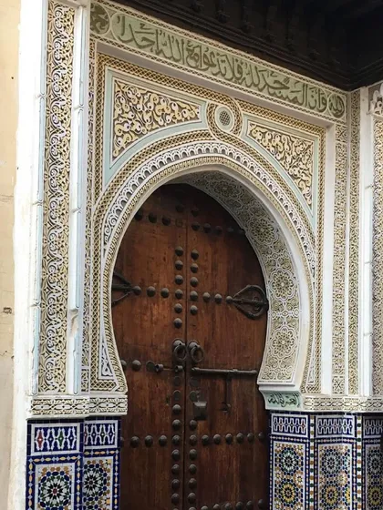 A classic Moroccan arched doorway, framed with intricate tile work (*zellige*) and carved plaster. The horseshoe-shaped arch is a prominent feature in Moroccan architecture, often believed to protect against the evil eye.