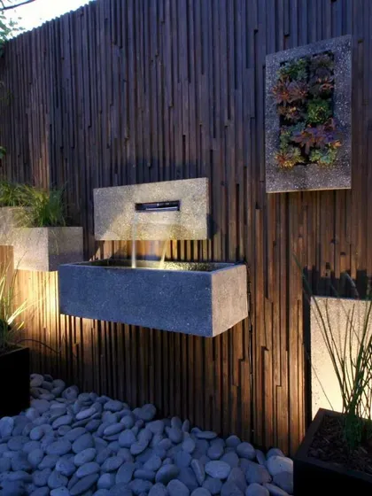 This modern garden wall combines a dark wood finish with several floating stone planters and a minimalist water feature. The subtle lighting highlights the different textures, creating a sophisticated and serene composition.
