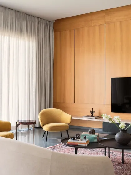 A corner of the living room at Amaiti Farmhouse, showing the interplay of textures. The smooth, cool Kota stone floor contrasts with the warm wood panelling, a soft Persian rug, and plush yellow armchairs, creating a balanced and inviting space.