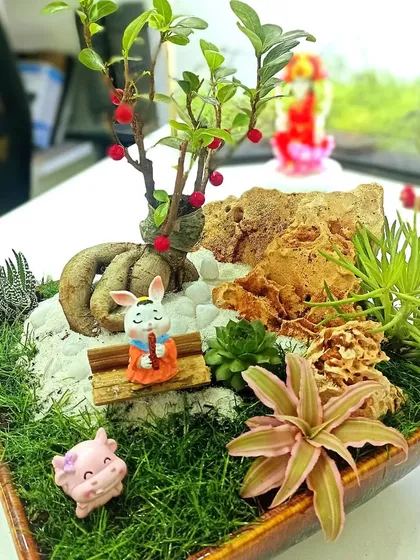 A custom-made miniature garden in a ceramic tray. This bonsai and succulent arrangement includes cute figurines for a playful touch.