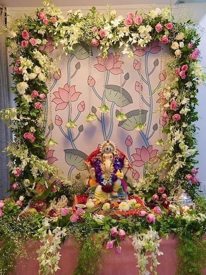 A fresh and natural Ganpati decoration featuring a lush arch of white and pink flowers with plenty of green foliage. The backdrop is a custom print of lotus flowers, enhancing the divine theme.