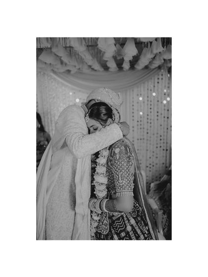 A deeply emotional black and white photo of a groom embracing a family member, capturing a moment of love and blessing during the wedding.