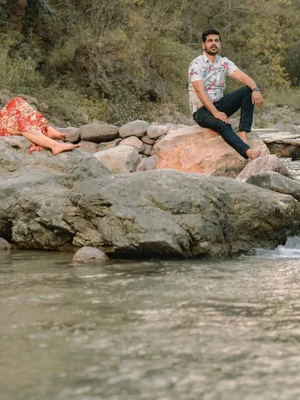 A full shot of the couple in a relaxed pose by the river, highlighting the beautiful natural location of their pre-wedding photography session.