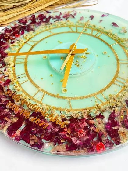 This 12-inch wall clock features preserved orchids against a light sea-green background. The purple and white flowers are complemented by delicate gold flakes.