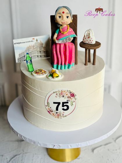 A personalized cake celebrating a grandmother's 75th birthday. The design includes a custom fondant figure and edible images of her favorite things, like her temple and snacks.