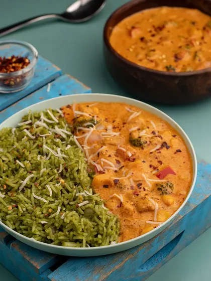 A colorful bowl of spinach rice with veggies in a tandoori sauce. The split-bowl presentation is visually interesting and highlights both components of the meal.