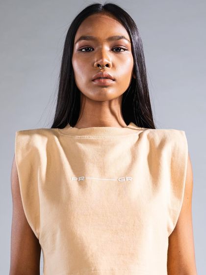 A full-face look from a fashion campaign, featuring neutral tones and a focus on skin texture. The hair is styled away from the face to highlight the makeup and the garment's neckline.
