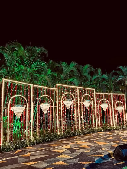 A unique Sangeet backdrop wall made of red bamboo sticks within illuminated geometric frames, combining natural and modern elements.
