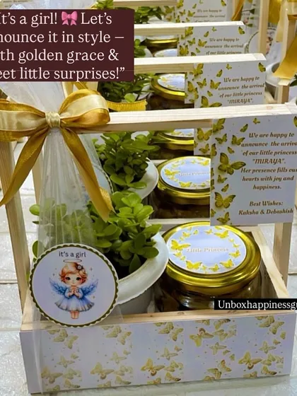 This close-up of the "It's a girl!" announcement basket shows the personalized card with the baby's name, the jade plant, and jars of treats, all tied with a golden ribbon.