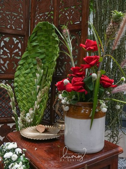 A close-up of the selfie booth's floral arrangement, with red roses and woven palm leaves against a carved wooden screen.