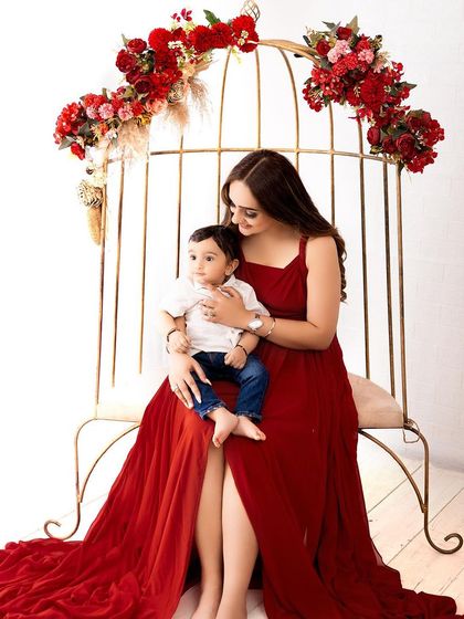 A mother and son portrait on an elegant, birdcage-style bench decorated with red flowers. The rich colors create a vibrant and luxurious feel.