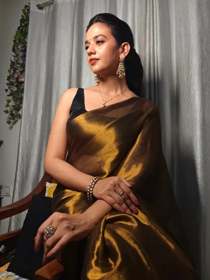 A seated portrait of Shruti Sharma, showcasing the beautiful drape and sheen of the Huts and Looms saree. The look is classic, timeless, and lets her natural grace shine through.