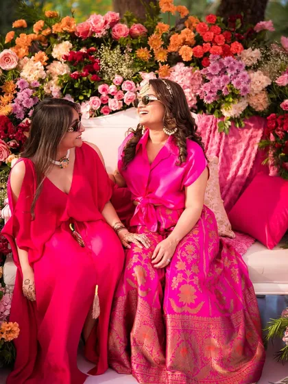 Two friends sharing a laugh on the floral Mehendi sofa. The vibrant colors of their outfits and the decor create a picture of happiness.