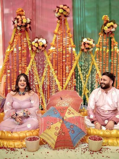 A lovely portrait of the couple seated together at their Haldi ceremony. The colorful decor with marigold flowers and traditional umbrellas creates a perfect backdrop.