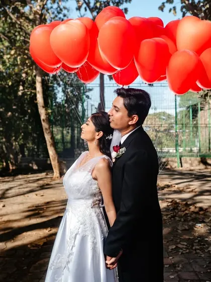 Using a bunch of red, heart-shaped balloons to create a colorful canopy over the couple. This is a simple but effective way to add a touch of whimsy and romance to a portrait.