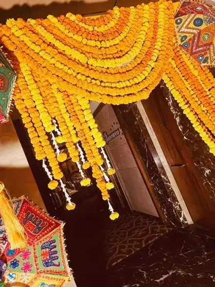 A festive entrance arch for a Mehendi party, heavily decorated with marigold garlands and colorful Rajasthani umbrellas and tassels. This creates a grand and traditional welcome for guests.