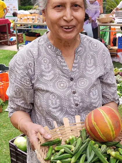 A customer with a basket full of fresh okra and a colourful striped melon.
