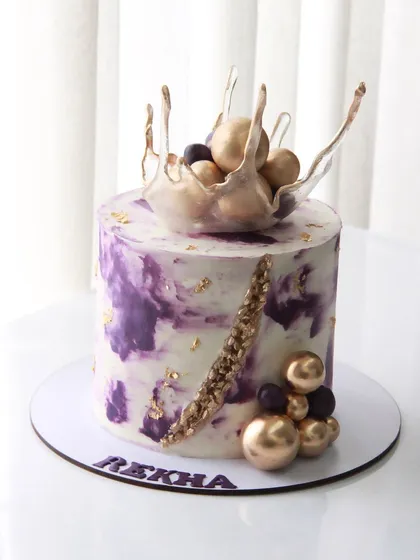 A tall cake in shades of violet for a 60th birthday. I created a marble effect with colored ganache and topped it with a delicate isomalt splash and gold chocolate balls.