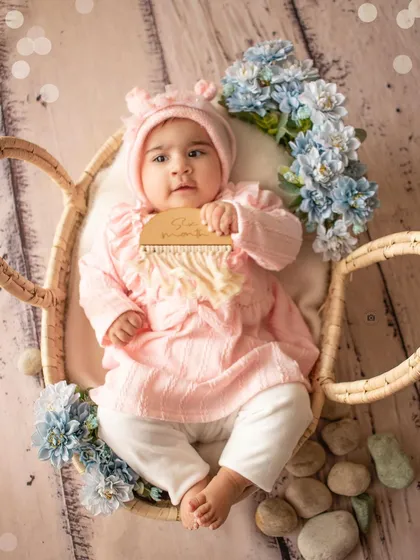A six-month-old baby girl holds a milestone plaque in a cozy basket setup with blue and pink floral accents.