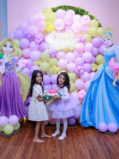 Two little princesses hold a gift in front of a beautiful balloon wall featuring Cinderella and Rapunzel. Our decor creates the perfect setting for all your treasured party photos.