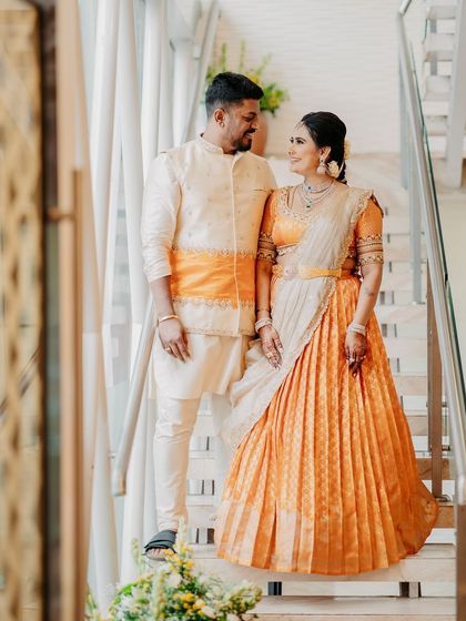 A classic portrait of the couple. His cream kurta with an orange sash matches her vibrant orange half saree, a perfect example of our coordinated designs.