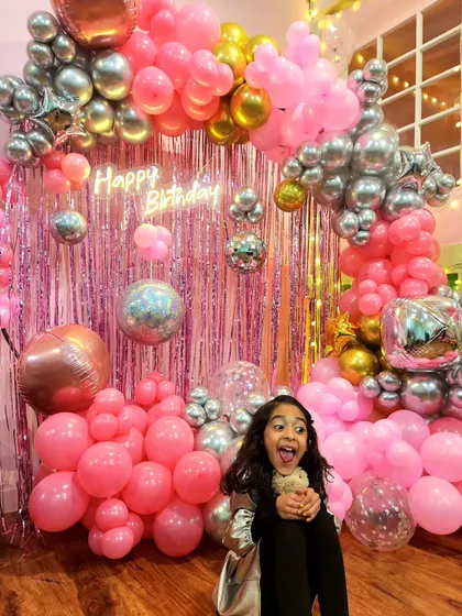 A party guest enjoying the shiny disco balls and vibrant pink balloon setup. It's all about creating an exciting and photo-worthy environment.