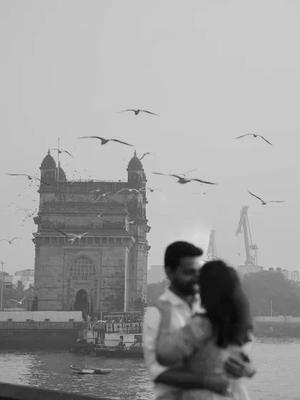 An artistic, blurry black and white shot focusing on the Gateway of India and the birds, with the couple as a romantic element in the foreground.