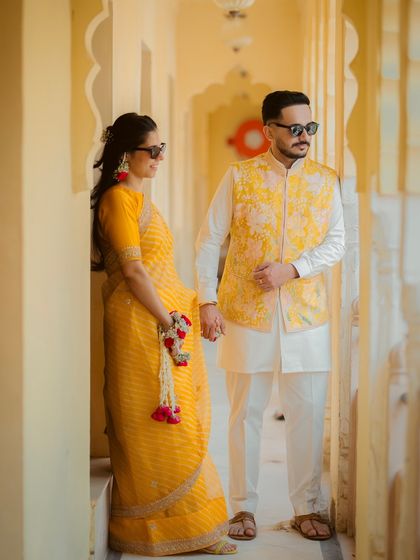A stylish couple portrait taken during their Haldi event, with both wearing coordinated yellow outfits and sunglasses.