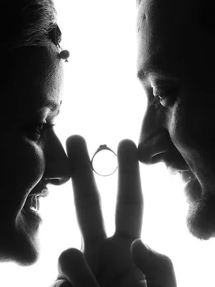 A creative black and white silhouette shot where a couple's faces are in profile, with their fingers forming a 'V' to hold up the engagement ring between them. This is an example of the unique and symbolic shots I love to create.