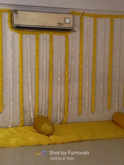 Another view of a simple home Haldi setup, with marigold strings and comfortable seating arrangements on the floor.
