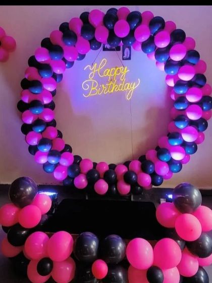 A bold and modern birthday decoration with a ring of black and hot pink balloons, lit from within for a glowing effect around the neon sign.