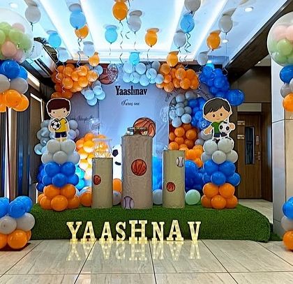 A sports-themed birthday party for a young football fan. The decor features balloon pillars, a custom backdrop, and character cutouts in a blue and orange color scheme.
