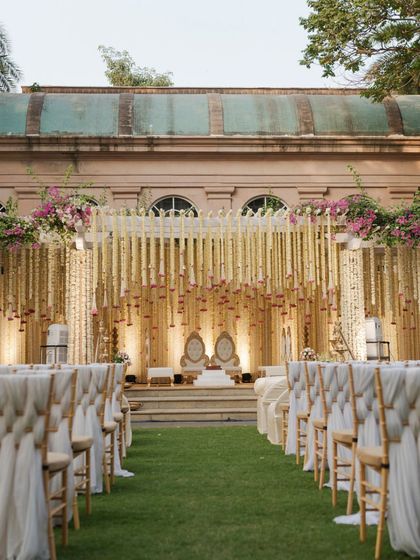 The wedding aisle, lined with elegant seating and leading to a mandap draped in fragrant rajnigandha strings, creates a path of classic, serene, and timeless beauty. This setup was designed for an outdoor wedding at a heritage venue in Mumbai.