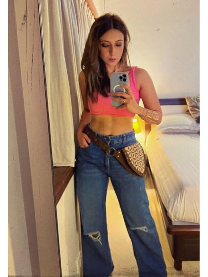 A casual mirror selfie. A bright pink crop top, baggy jeans, and a unique belt bag make for a fun, everyday look.