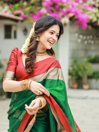 Bright and cheerful outdoor portraits of an actress in a vibrant green and red saree. The natural lighting and blooming flowers in the background complement her radiant smile.
