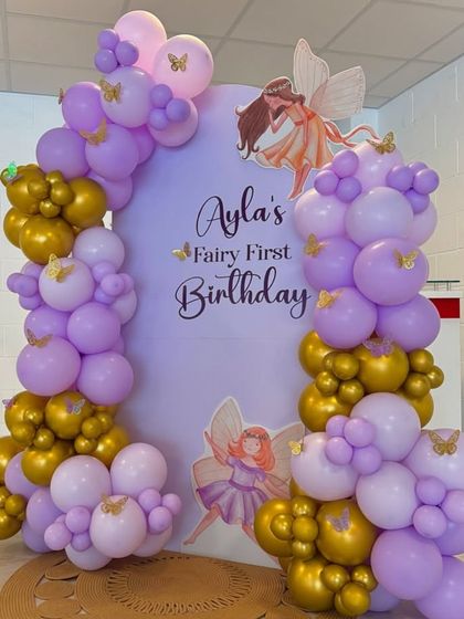 A 'Fairy First Birthday' theme with a purple and gold balloon garland framing a custom arched backdrop.