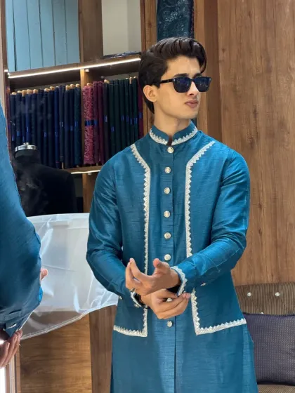 This teal blue layered kurta set is a modern take on traditional wear. The outer layer has a unique cut and white piping detail, making it a stylish choice for weddings or festive parties.