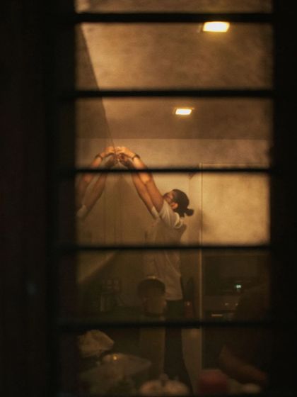 A candid shot from behind a window, capturing a quiet moment of hard work in the kitchen late at night.